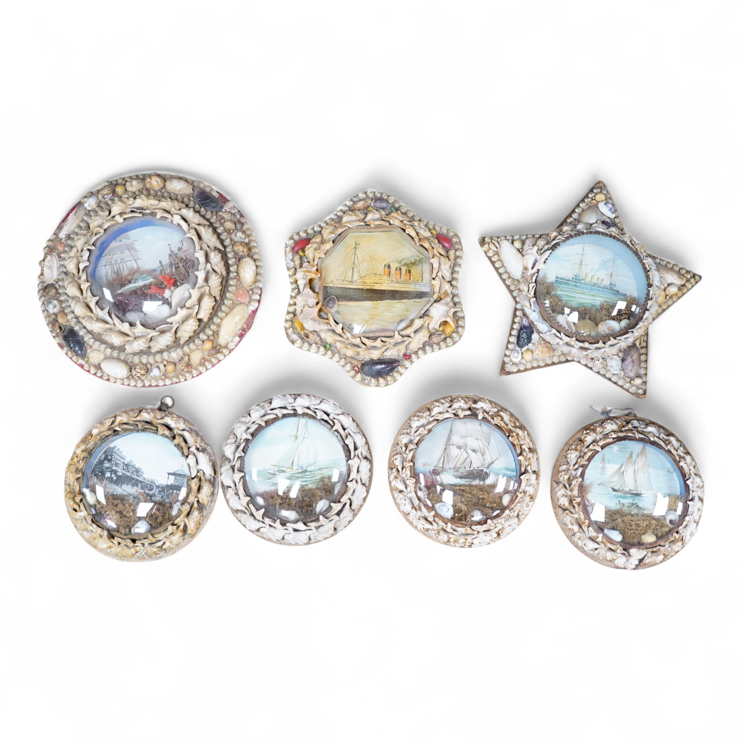 A collection of seven shellwork frames with convex glass, housing maritime interest prints with seaweed and shell decoration, largest 23cm in diameter